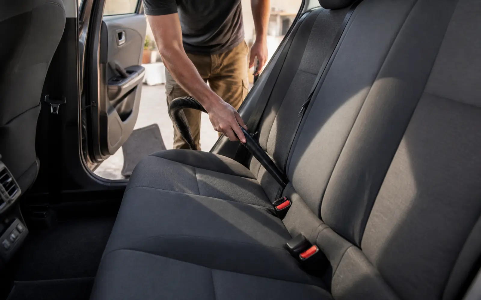 Persona aspirando con una boquilla estrecha la unión del asiento trasero de un coche