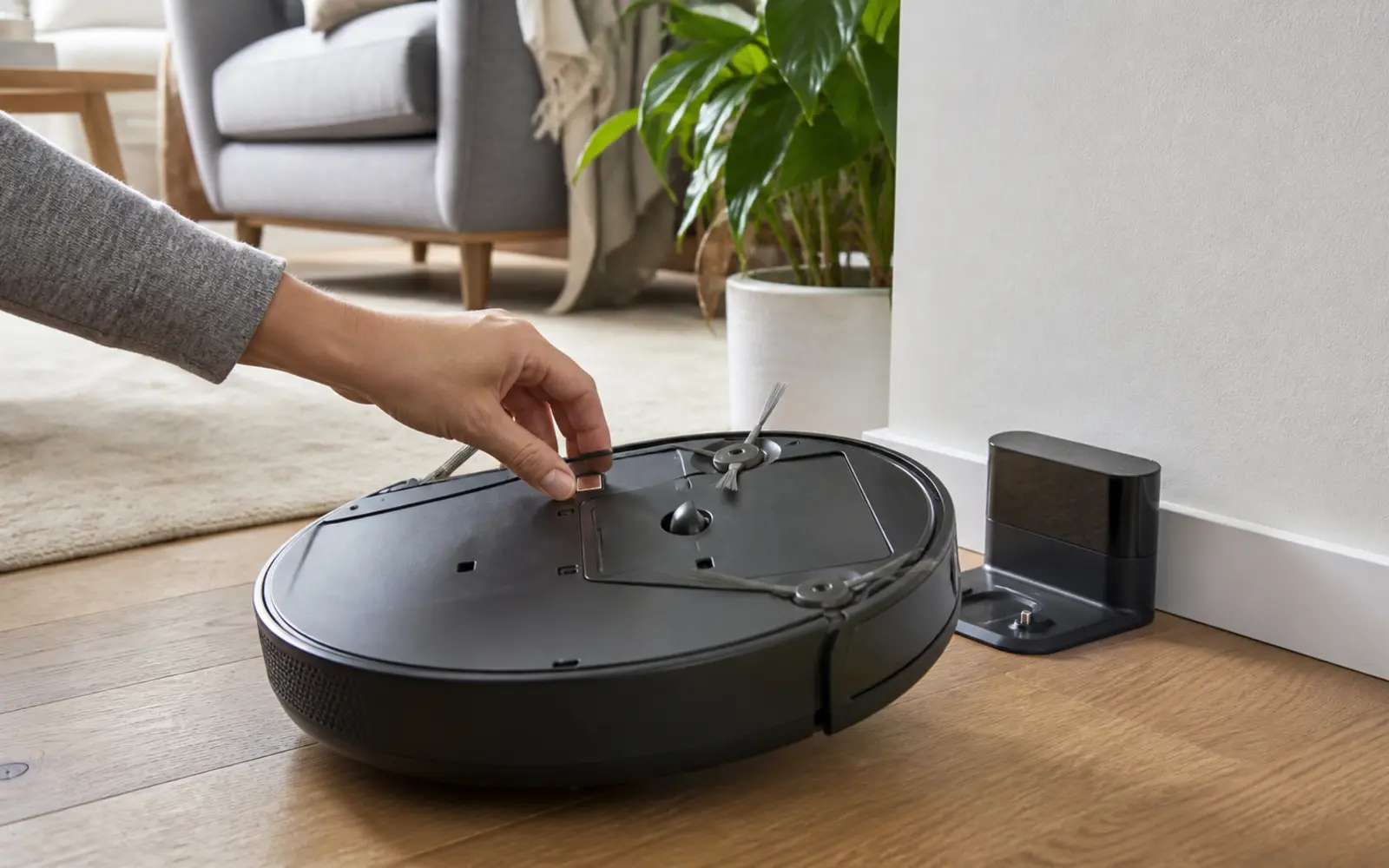 Persona inspeccionando los contactos inferiores de un robot aspirador junto a su base de carga